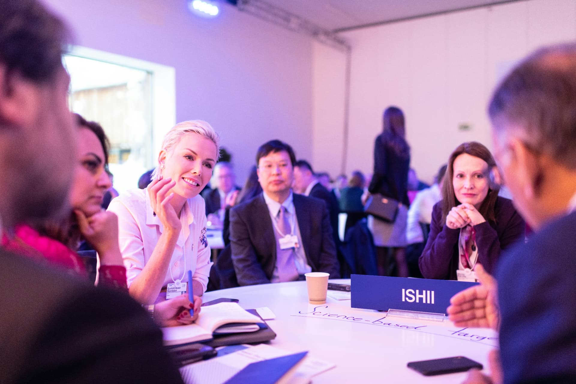 Deltakere i samtale ved et rundt bord under et større seminar