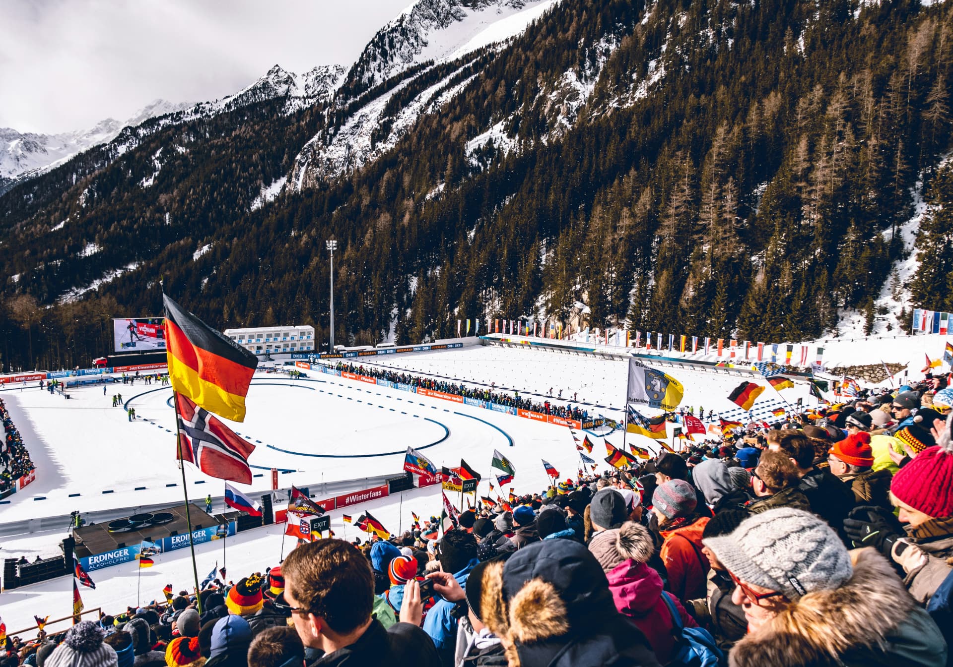 Publikum med flagg på tribunen under et internasjonalt skiskytterarrangement i Alpene